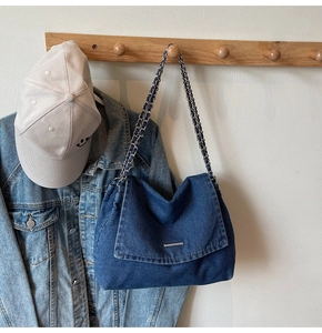 Detailed view of dark blue denim tote bag with chain strap hanging on wooden wall hook