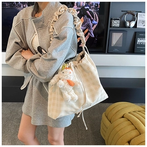 Detail of checkered drawstring bucket bag with a plush bunny charm and ruffled strap