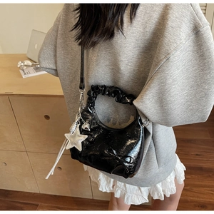 Detail of black patent leather bag with ruched handle and silver star pendant accessory