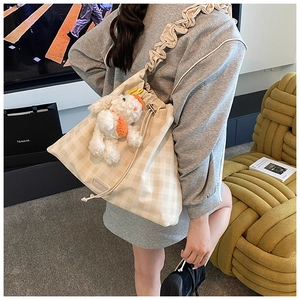 Detail of checkered tote bag featuring ruffled strap and cute plush charm in cozy setting