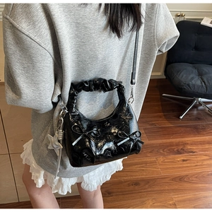 Detail of black patent leather hobo bag with ribbon bows and silver star charm pendant