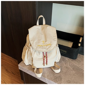 Dettaglio dello zaino in tela beige con ricamo giallo e nodi decorativi sulla tasca