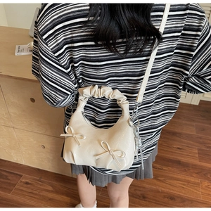 Detail of creamy white patent leather bag with ruffled handle and silver heart charm
