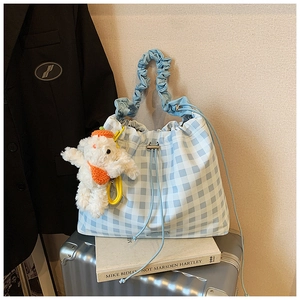 Close-up of blue gingham drawstring bag with plush bunny charm on a silver suitcase