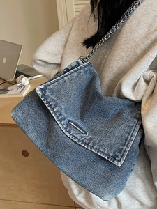 Blue denim tote bag with silver chain strap and metal trim in a casual lifestyle setting