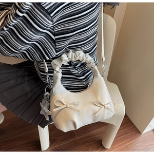 Close-up of pleated cream shoulder bag with twin bow details and star charm accessory