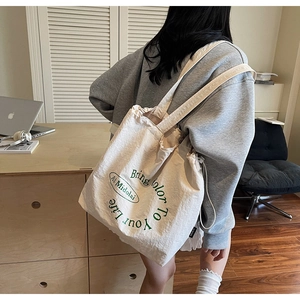 Detail of beige canvas tote bag with green lettering shown in a modern lifestyle setting