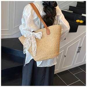 Detail of woven straw tote bag featuring white floral lace bow and brown leather shoulder strap