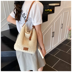 Detail of hollow-out woven tote bag featuring brown leather straps and branded label