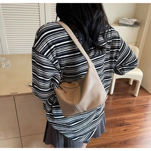 Gros plan d'un sac hobo kaki en cuir souple porté par un mannequin dans un cadre cosy