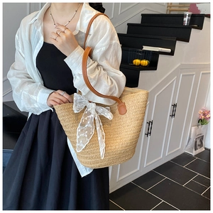 Detail of woven straw tote bag featuring brown leather strap and white lace bow accent