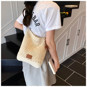 Detail of hollow woven beige tote bag featuring a brown leather logo patch on surface