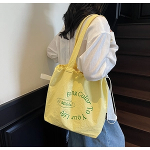 Detail of a bright yellow drawstring tote bag featuring green printed text and textured fabric