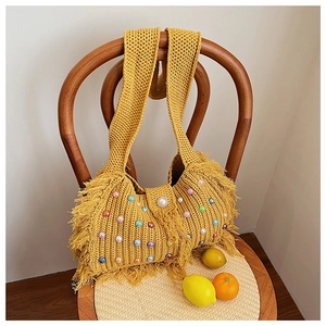 Détail d'un sac en tricot jaune avec perles colorées et longues franges sur une chaise