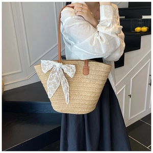 Detail of beige woven tote bag featuring a large white lace bow and brown leather strap