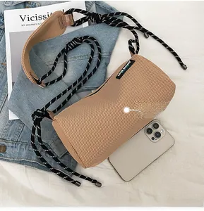 Cylindrical mesh crossbody bag in khaki with cord strap, shown next to a smartphone