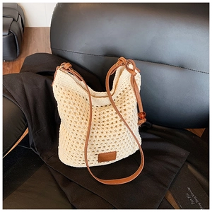 Close-up of beige woven hollow bucket bag with brown leather logo patch and strap details