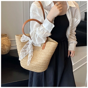 Detail of woven straw tote bag featuring a white lace bow and brown leather handles