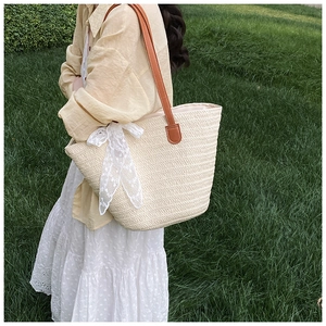 Detailed view of the woven straw tote bag with elegant lace bow and leather strap