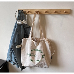 Detail of cream canvas tote bag with drawstring closure and green text hanging on a hook