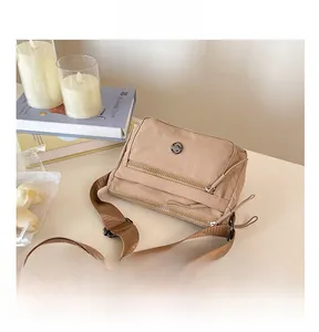Detail view of a light brown nylon crossbody bag with multiple zippers and adjustable strap