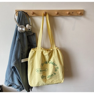 Detail of yellow canvas tote bag with drawstring closure and green text print