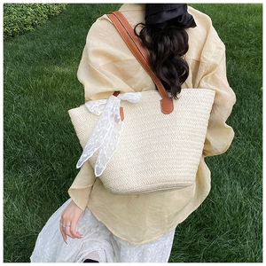 Detail of woven straw tote bag with white lace bow and brown leather strap on grass