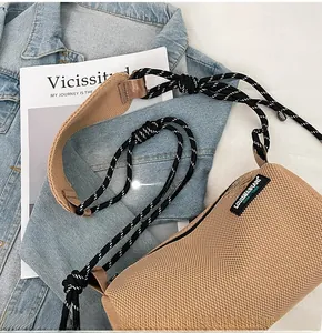 Detail of tan mesh crossbody bag with woven shoulder strap and brand label on side