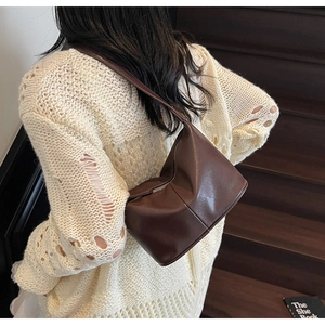 Sac bandoulière géométrique café foncé porté avec un pull en maille blanc sur escalier