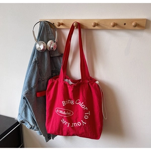 Detail of red drawstring canvas tote bag with white lettering on a minimalist wall hook