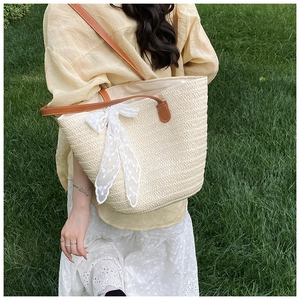 Close-up of beige woven straw tote bag with brown leather straps and white lace ribbon