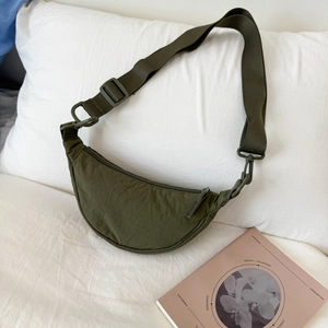 Detailed close-up of the olive green nylon crescent bag on a white pillow with soft lighting