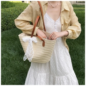 Detail of woven straw tote bag with brown leather handles and white lace bow decoration
