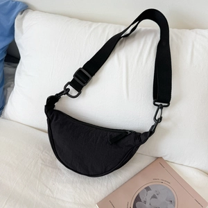 Detail of black nylon crescent bag with adjustable wide strap on casual bedding background