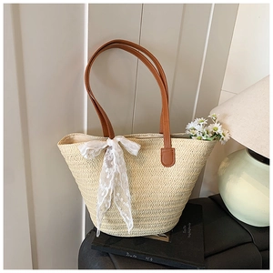 Detail of woven straw tote bag with brown leather handles and decorative white lace bow