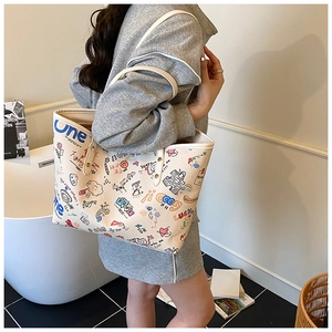 Close-up of beige tote bag with colorful doodle prints worn on shoulder in a modern setting