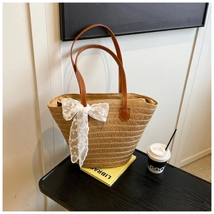 Detail of hand-woven straw tote with brown leather handles and a large white lace bow