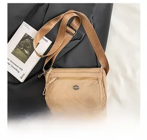 Detail of beige nylon crossbody bag showing multi-zipper compartments and metallic logo