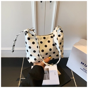 Chic white hobo bag with large black polka dots held by a model in a minimalist setting