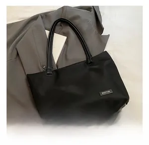 Detailed close-up of a black minimalist tote bag with a metallic logo plate on the front