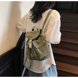 Detailed back view of a green plaid fabric backpack with white buckle on wooden stairs