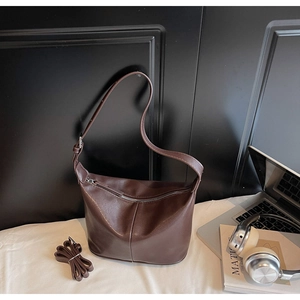 Détail du sac hobo en cuir marron foncé avec bandoulière à côté d'un livre d'art