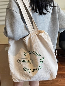 Minimalist cream canvas tote bag with drawstring closure and green letter print