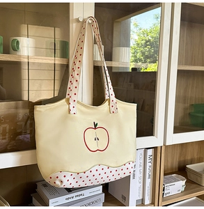 Close-up of beige tote bag with apple print and red polka dot straps on wooden cabinet