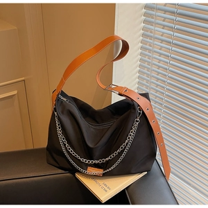Close-up of black nylon tote bag featuring orange leather strap and silver chain details