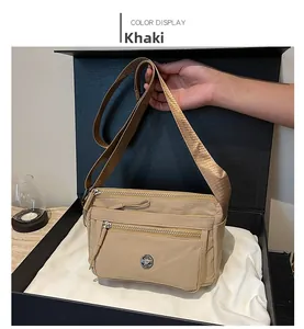 Detail view of khaki nylon crossbody bag with multiple silver zippers in gift box