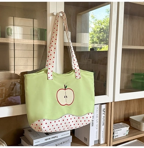 Detail of light green canvas tote bag featuring red apple embroidery and polka dot straps
