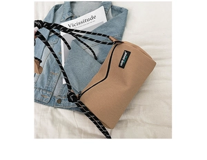 Close-up of brown textured cylinder bag with logo tag and woven rope shoulder strap