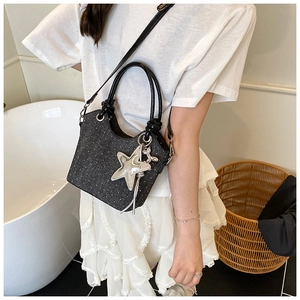 Detail view of dark grey polka dot bucket bag with star and rabbit charms on a long strap