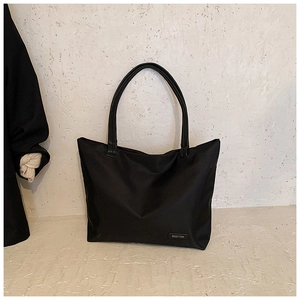 Detailed close-up of a minimalist black tote bag featuring a brand label on nylon fabric